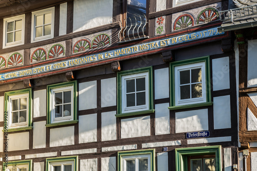 Obraz na plátne Detailed close-up of an ornate 16th-century half-timbered house in Goslar, Germany, featuring colorful carved decorations, green window frames, and a Latin carved inscription on Peterstraße