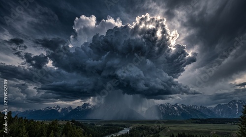Ominous Storm Cloud Formation Over Mountains: A dramatic storm cloud, illuminated by piercing sunlight, looms over a majestic mountain range, bringing a sense of awe and impending change.