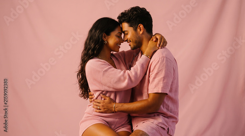 Couple in pink loungewear embracing and gazing at each other against a soft pink studio background.