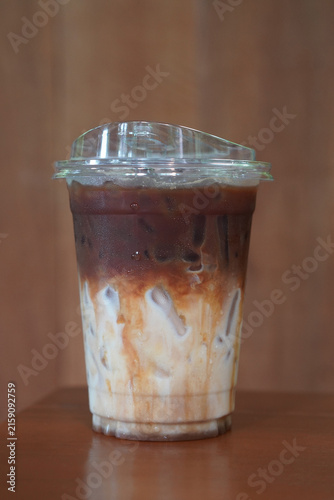 front view closeup cool and ice coffee and caramel Macchiato drink in a clear plastic cup, on wooden floor, brown wooden wall background, drink, cool, copy space