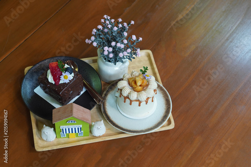 top view macadamia coffee cake and chocolate cake in ceramic plates and vase of pink flowers and decorative on a wooden tray placed on a wooden floor background, food, sweet, copy space
