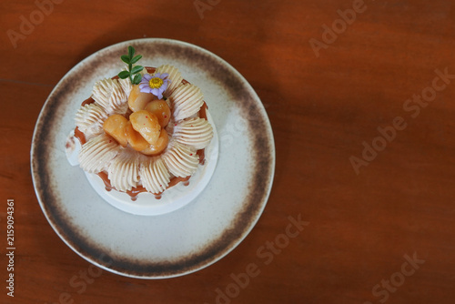 top view mini macadamia caramel and coffee cake and decorated with flowers, whipped cream, and macadamia nuts served on brown and white ceramic plate on wooden floor background
