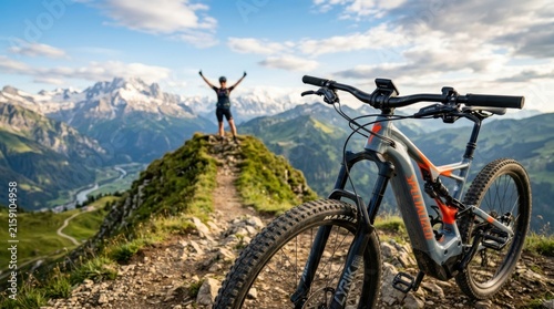 Cyclist celebrates mountain summit success with arms raised against alpine backdrop on e-bike adventure