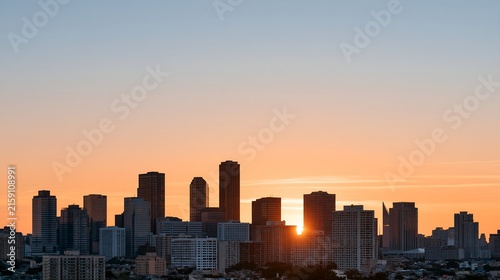 Sun dips behind city skyline, casting warm hues.