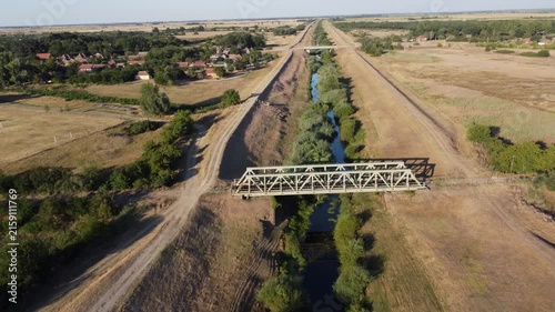 Wide aerial shot of a long iron truss railway bridge spanning a wide river in a lush green countryside. Landscape structure crossing water nature 
