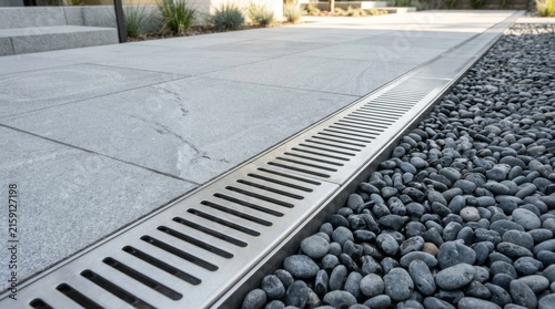 Modern concrete patio with integrated metal drainage system and decorative stone border.