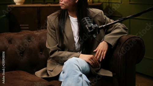 Woman sitting on a leather couch, recording a podcast with a studio microphone