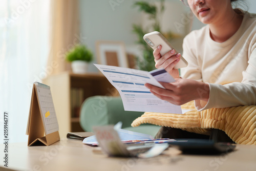 фотографія Woman checking household bills with smartphone and payment card at home, concept