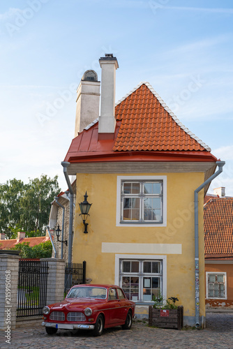 Red classic vintage car parked in front of a yellow historic house in Tallinn old town