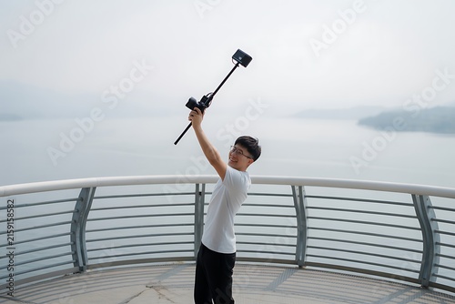 Young Asian Content Creator Holding Camera on Monopod Extension Pole Above Lake
