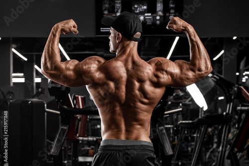 Muscular man showing back musclesin gym. Strong male rear view