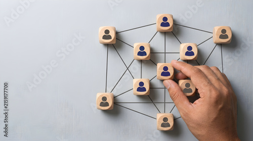 Wooden cubes with human icons arranged in a network structure managed by a human hand closeup