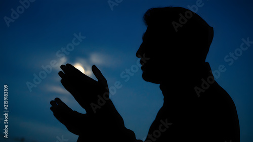 Fotografía Devout muslim man stands in profile silhouette against deep blue night sky while