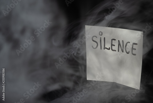 Bild auf Leinwand White sticky note with handwritten word SILENCE in dramatic swirling smoke on dark background