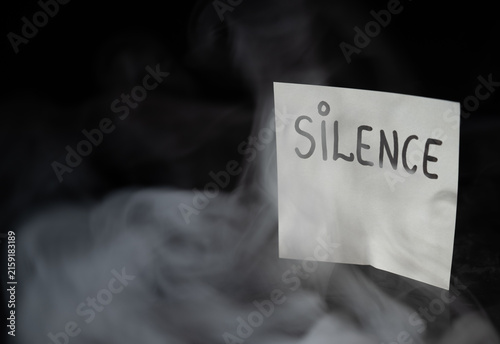 Fotografía White sticky note with handwritten word SILENCE in dramatic swirling smoke on dark background