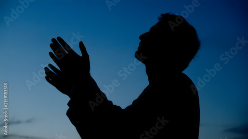 Fotografie Devoted man standing in silhouette against a clear deep blue twilight sky while