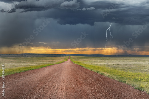 A remote road in the arid great plains framed by a large storm signifies the remote and harsh climate of the region 