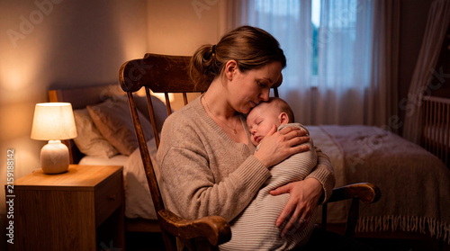 Loving mother holding her sleeping newborn baby affectionately in a cozy rocking chair in a dimly lit nursery, peaceful motherhood moment, gentle family care, relaxing night routine.
