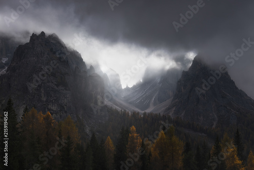 View of the dramatic rocky peaks of Tre Cime di Lavaredo rising above the autumn larch forest near Lake Antorno in Auronzo di Cadore, Veneto, Italy.