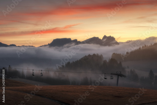View of Alpe di Siusi with a chairlift silhouetted against a misty mountain landscape during a golden sunset in Bolzano, Trentino-Alto Adige, Italy.