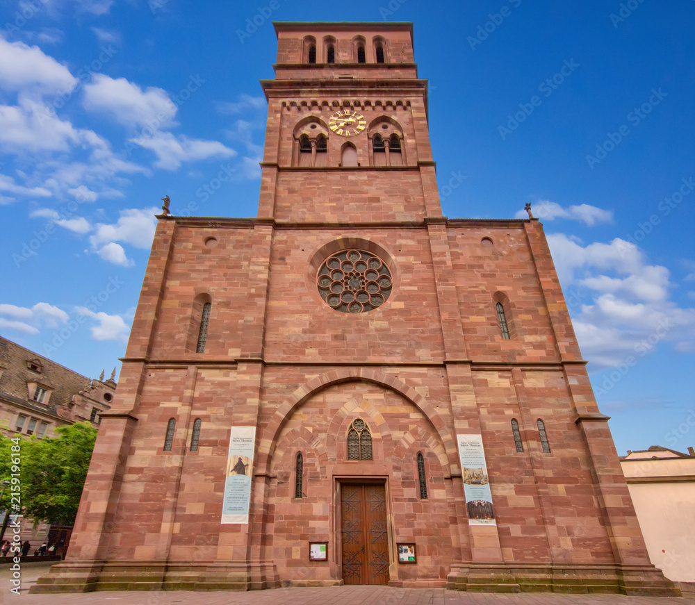 Fototapeta premium Exterior view of Saint Thomas Church in Strasbourg, France, featuring its monumental red sandstone facade, Gothic architectural elements, large rose window, and prominent square clock tower.