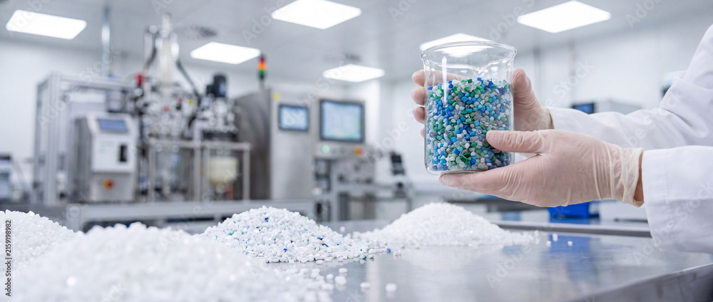 Fototapeta premium Laboratory technician holding jar of plastic pellets in cleanroom polymer production quality control facility