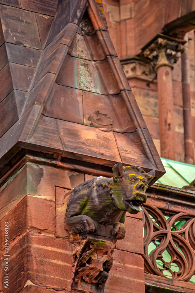 Fototapeta premium Close-up view of a grotesque gargoyle on Strasbourg Cathedral, surrounded by Gothic stone sculptures, carved columns and architectural ornamentation in Strasbourg, France.