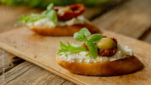 Photography Bruschetta or crostini with cream cheese, sun-dried tomatoes, olives, fresh basil leaves and lettuce