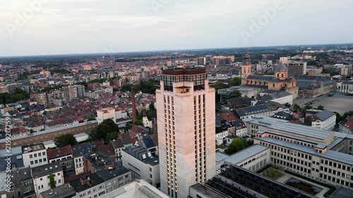 Aerial drone footage orbiting the Book Tower (Boekentoren) of Ghent University above the rooftops of Ghent Belgium in warm evening light a scenic view of the modernist city landmark.