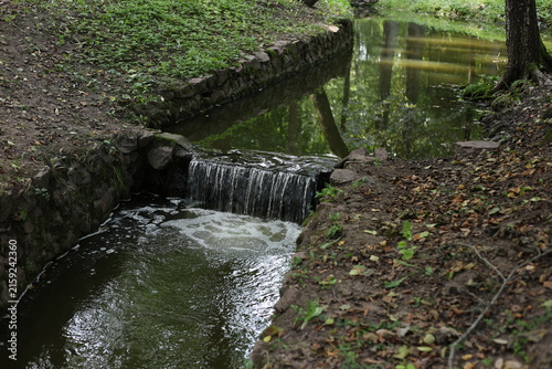 Scenic view of a small stone weir waterfall with crystal clear flowing water and foamy pool in a peaceful park stream.