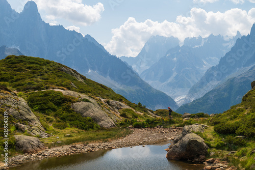 Rocky alpine tarn and hiking path overlooking dramatic Mont Blanc peaks in summer, Chamonix, France.