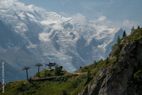 Snow-covered Mont Blanc massif rising above an alpine cable car and green mountain slopes in summer near Chamonix, France.