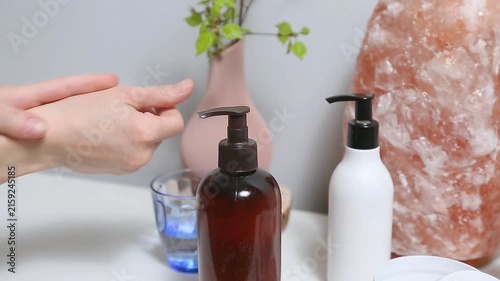 Woman performing a relaxing hand and wrist self massage as part of a wellness and self care routine at home. Female applying cream from product bottle to care moisturizing her palms skin