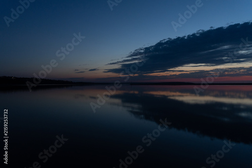 Bild auf Leinwand Serene Blue Hour Twilight Sky with Dark Clouds Perfectly Reflected on Glassy Sti