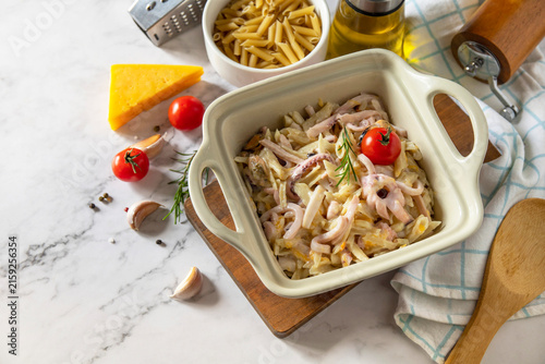 Savory homemade penne pasta with seafood in creamy cheese sauce on marble countertop. Copy space.