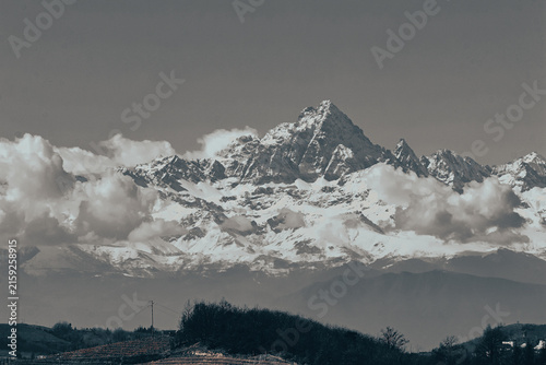 Scenic view of Monte Viso rising above the Asti hills, partially hidden by clouds. Retro colors create a nostalgic atmosphere, highlighting the contrast between the distant mountain, Piedmoте