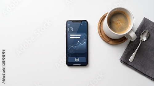 Smartphone displaying financial data next to a cup of coffee and spoon on a white table