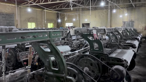 Interior view of a textile weaving factory multiple rows of mechanical power looms producing white fabric,