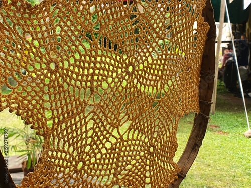 Close-up view of a handmade macrame or crochet hanging chair made from thick golden-brown rope or yarn. The intricate open-weave pattern creates a lacy, net-like texture with diamond and circular