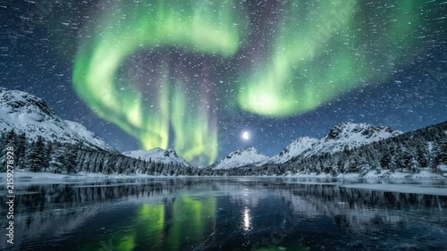 Spectacular Aurora Borealis over a tranquil frozen lake surrounded by snow-capped mountains at night.