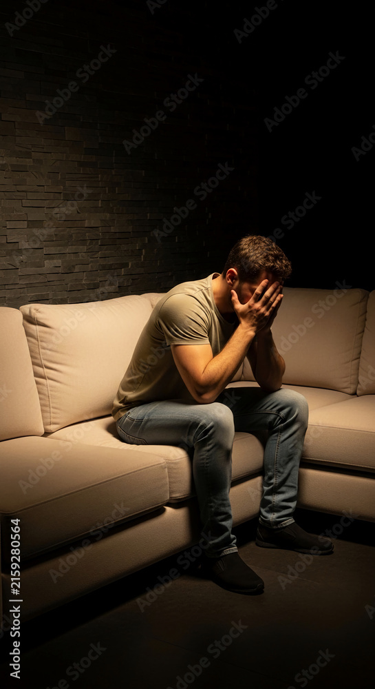 Fototapeta premium Man sitting on couch with face in hands, conveying a sense of despair or deep thought, symbolizing mental state, loneliness, or stress