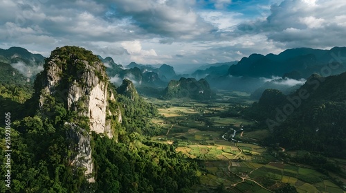 Dramatic karst landscape with lush green fields and misty mountains under a cloudy sky