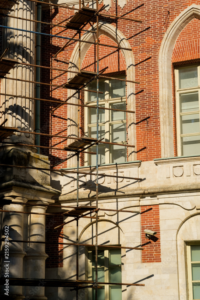 Fototapeta premium Scaffolding is positioned against a historic brick building featuring large windows and intricate architectural details in Tsaritsyno Park, Moscow