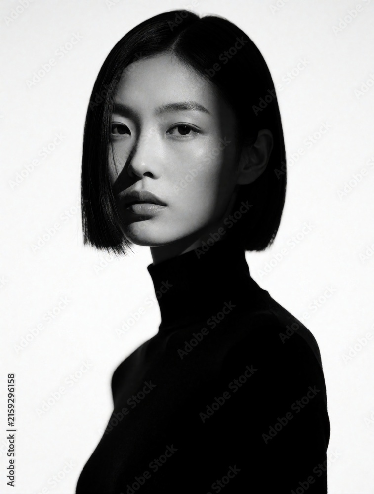 Fototapeta premium Young asian woman stylish bob haircut black turtleneck minimal beauty portrait. Sharp light shadows create dramatic moody aesthetic. High fashion editorial style.
