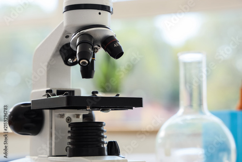 Modern laboratory microscope with multiple objective lenses and a glass flask...