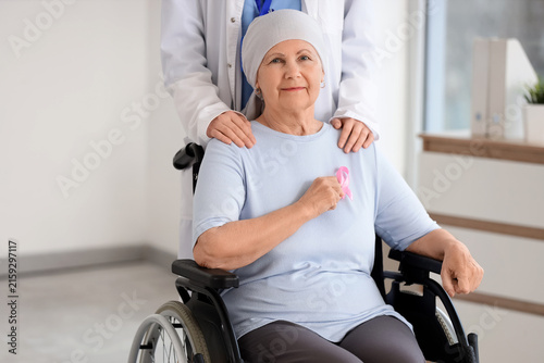 Senior woman in wheelchair after chemotherapy with pink ribbon and doctor at ...