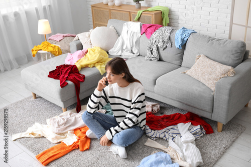 Beautiful young happy woman with different scattered clothes talking by mobil...