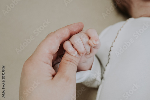Softly cupped infant fingers within caring parent palms. Delicate baby hand cradled tenderly by experienced adult hands in soft lighting. Gentle parental contact creates safe haven.