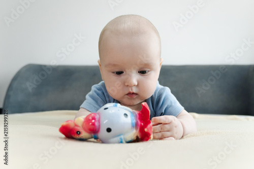 Baby boy lying on bed and gripping teething ring with both hands. Child chewing toy for teething relief. Exploring textures while soothing sore gums. Sensory discovery at home 