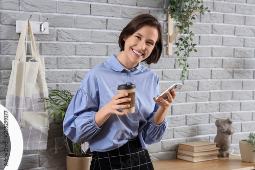 Female student with coffee cup using mobile phone at home